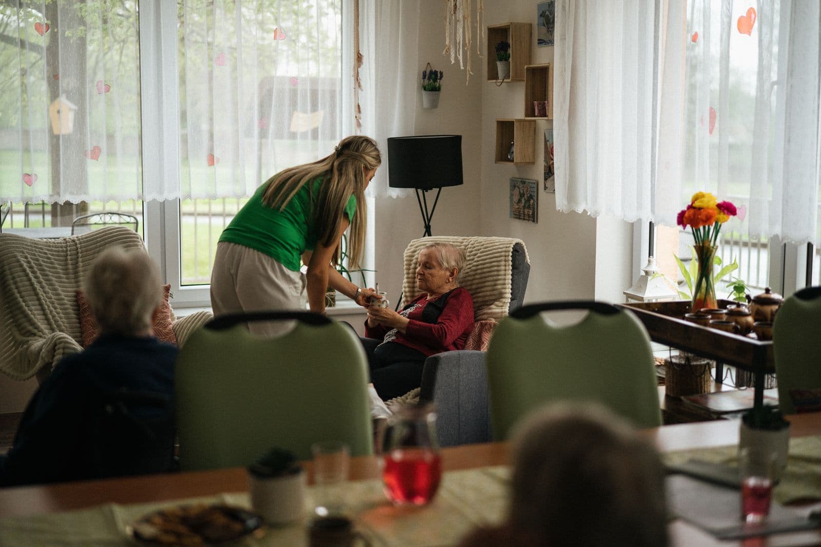 A caregiver serving tea to an elderly woman in a warm, comfortable home setting